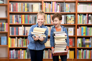 lachende Kinder mit Büchern im Arm vor vollem Bücherregal